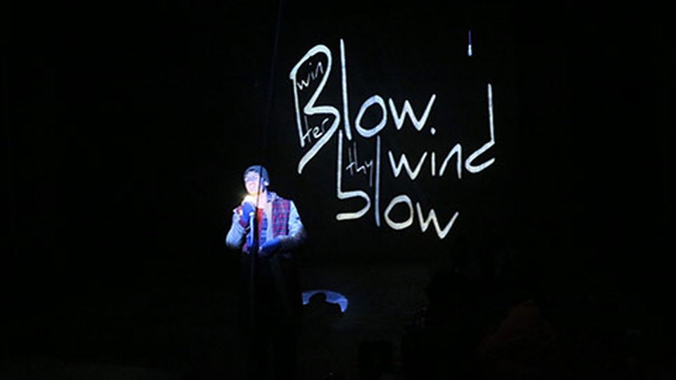 Student performing in front of black wall with words 'Blow wind blow' written in white