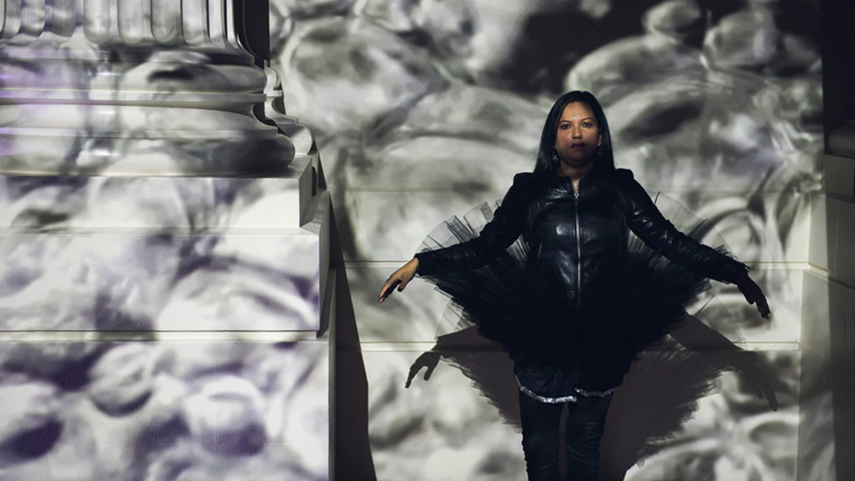 A woman dressed in black in front of a white projected background