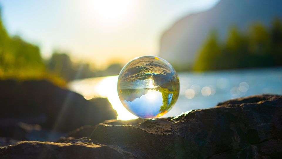 A glass ball balanced on a rock and reflecting the light of the lake behind it