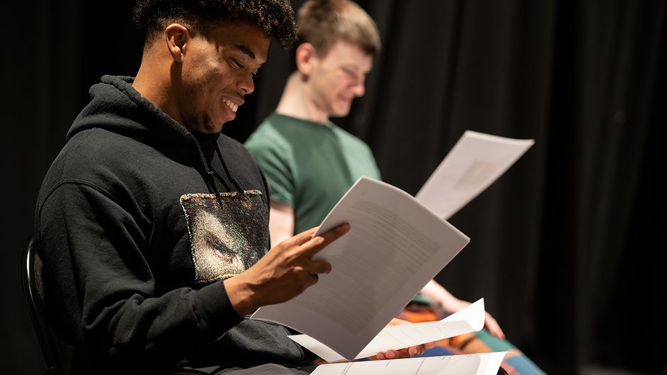 Two young men reading a script and smiling