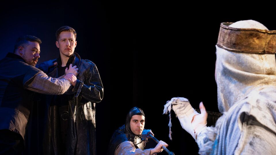 Production still of actor Rhys Anderson performing as Hamlet standing on stage with other members of the cast