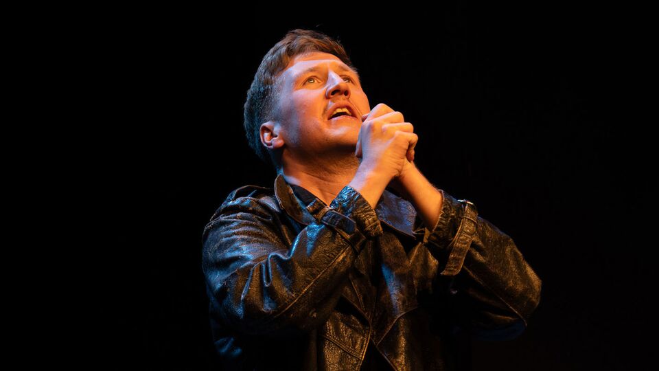 Production still of actor Rhys Anderson performing as Hamlet on stage with his hands out in prayer
