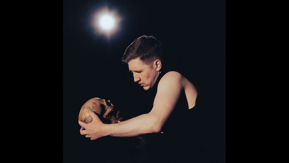 Production still of actor Rhys Anderson on stage holding a skull