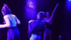Blurry image of women dancing ecstatically, the lights are all purple, and the women are only seen from behind.