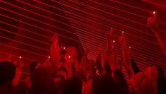 Several people hold their hands aloft and red lights and lazers interact with their bodies
