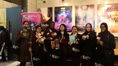 Several Mulberry Arts students hold books and toys and tote bags in front of theatre posters