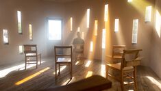 1.	A room with five brown chairs and a person sitting, illuminated by rays of sunlight coming through thin, tall rectangular windows across the walls.
