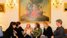Nuria Espert sits together talking with a group of actors underneath a large painting 