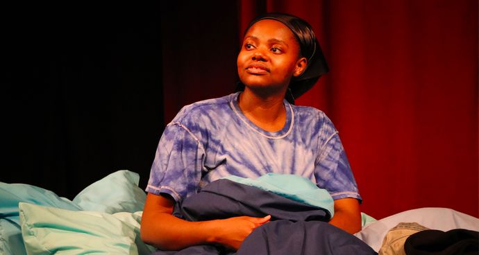 Photo from set of Patricia Gets Ready showing alumna Angelina Chudi sitting on a bed looking up