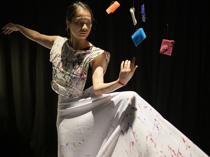 Performer in white dress with coloured objects floating before her