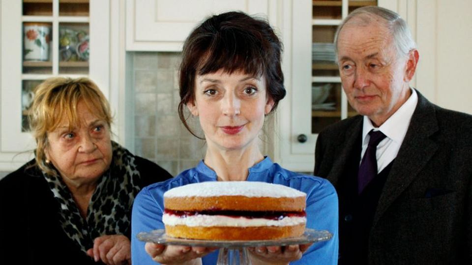 A woman holding a cake in front of a man and a woman