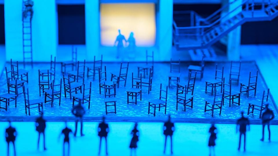 Miniature scene of figurines and chairs arranged on a stage in blue light