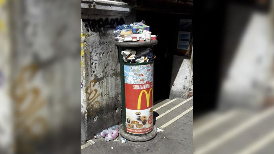 An overflowing public trash can in Italy