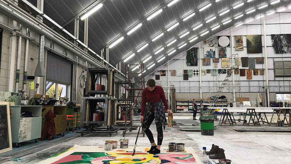 A large space with a painter standing over a very large artwork