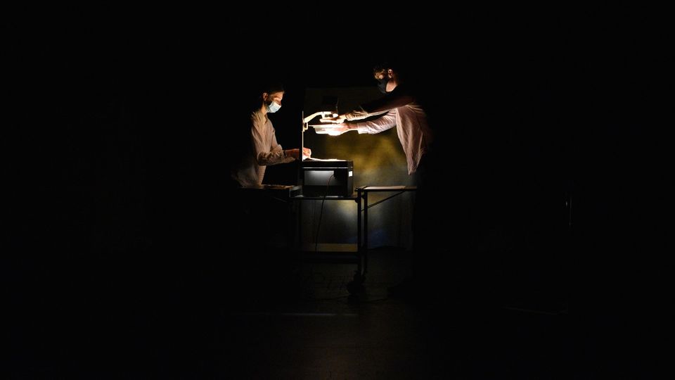 Performers wearing face masks, looking down at an over-head projector