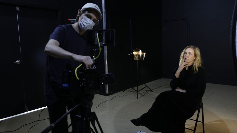 A camera man recording an actress who is sat on a chair