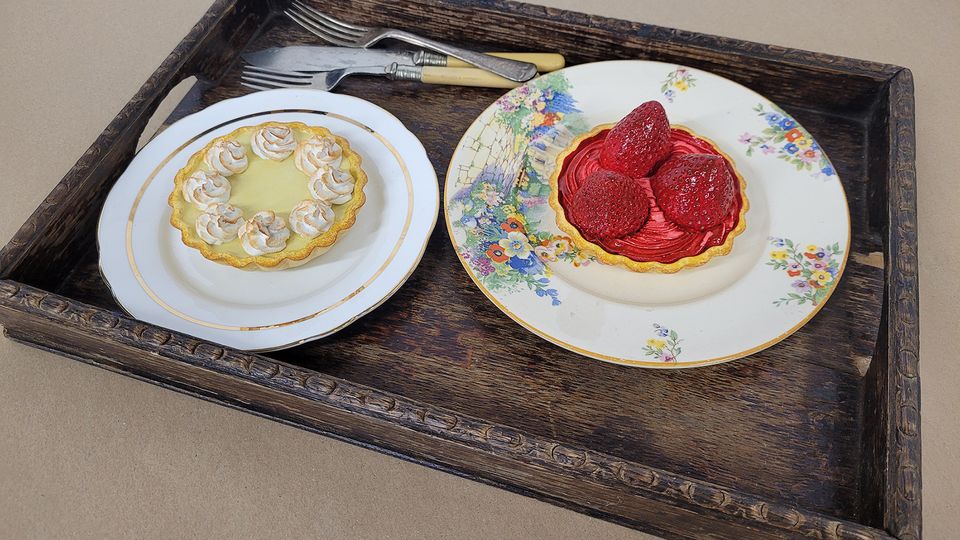 Realistic prop lemon meringue pie and strawberry tart on plates on wooden tray