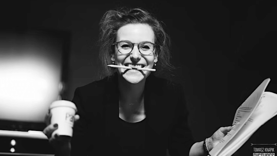 Black and white portrait of Magdalena Mosteanu holding a pencil between her teeth, and a coffee cup and papers in hands