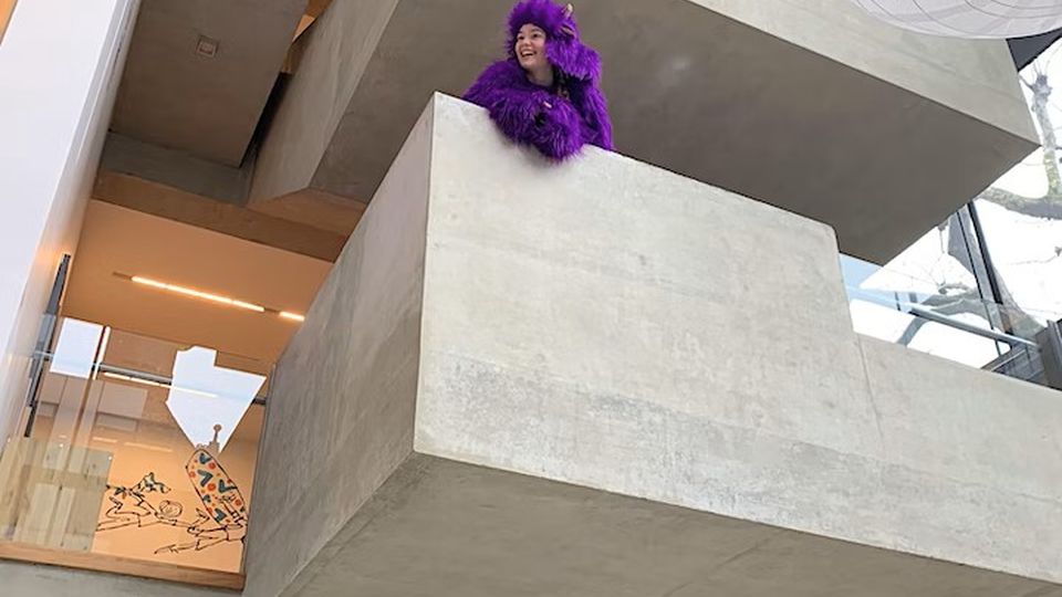 Anna Woolf leans across a brutalist indoor balcony 