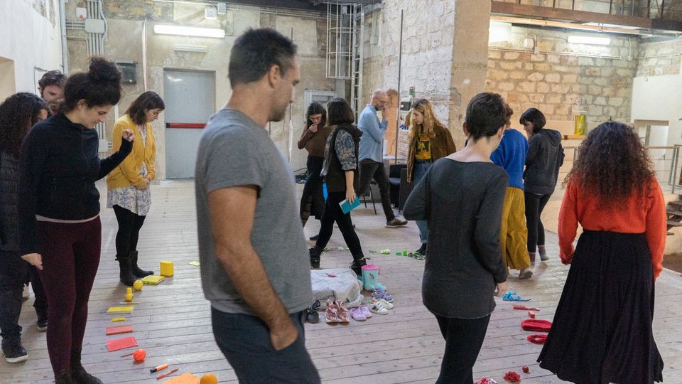 Participants walking around a theatre space interacting with a range of different objects arranged in a circle by colour