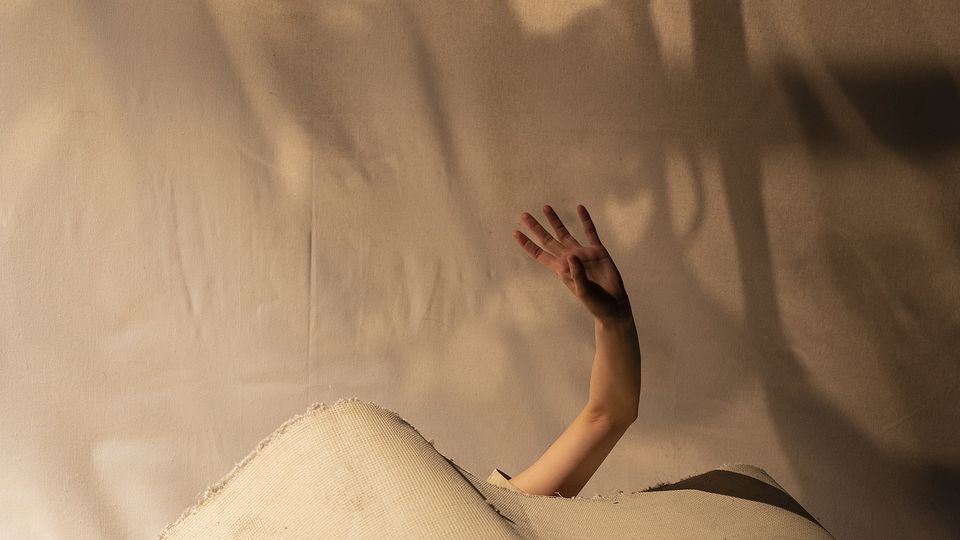 A hand reaches out from fabric against a shadowy wall