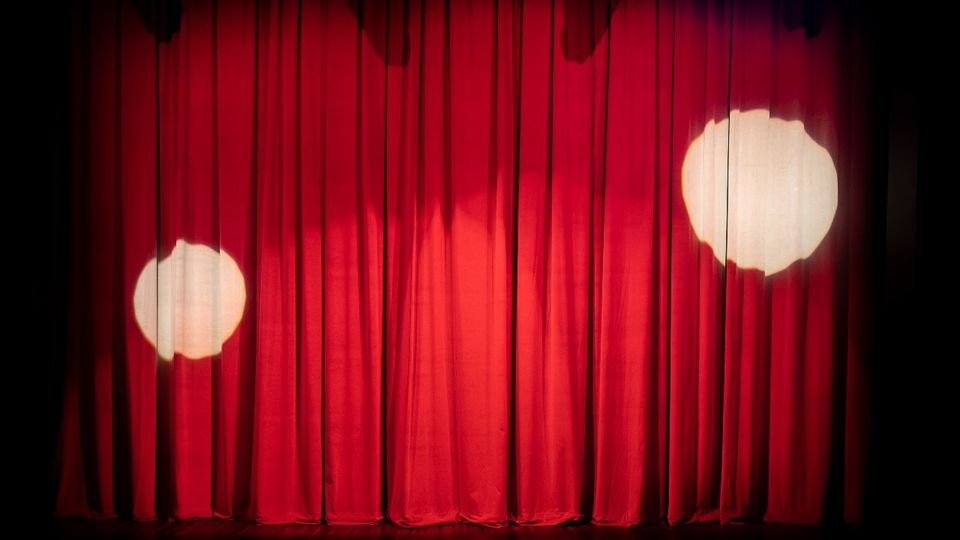 Red curtains on a stage with two white spotlights shining on them