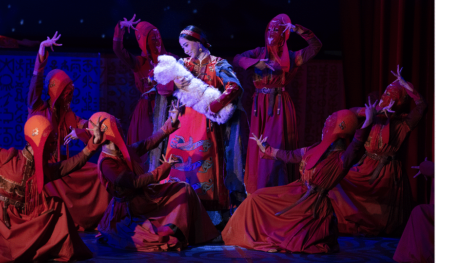 Production still from The Mongol Khan featuring a lady on stage surrounded by dancers
