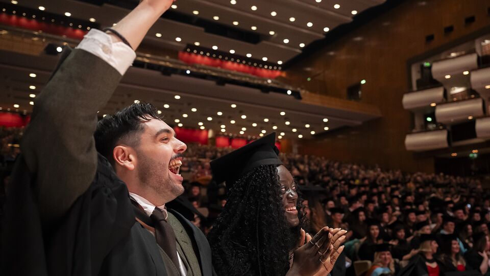 Two Central graduates stand in their caps and gowns in the auditorium of the Royal Festival Hall, celebrating