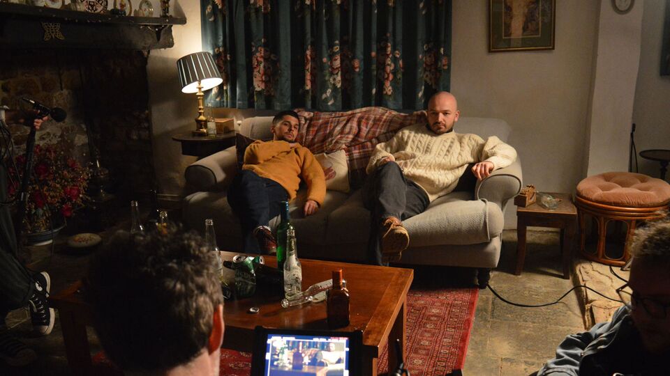 On set: Gabriel Mansour and Kristóf Gellen filming Beltane, they are both lying back on a coach in a living room looking at the camera