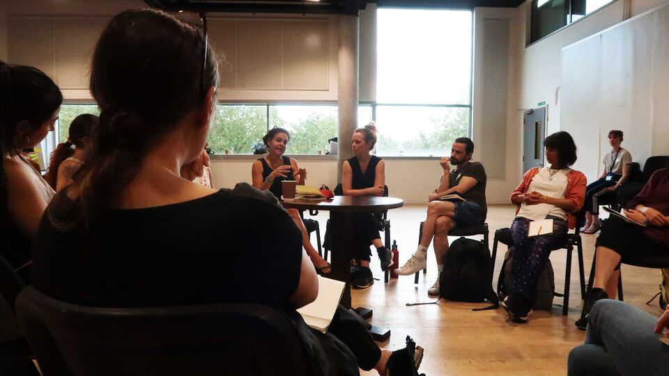 A group of movement practitioners seated on chairs in a rehearsal space, in a circle to facilitate discussion