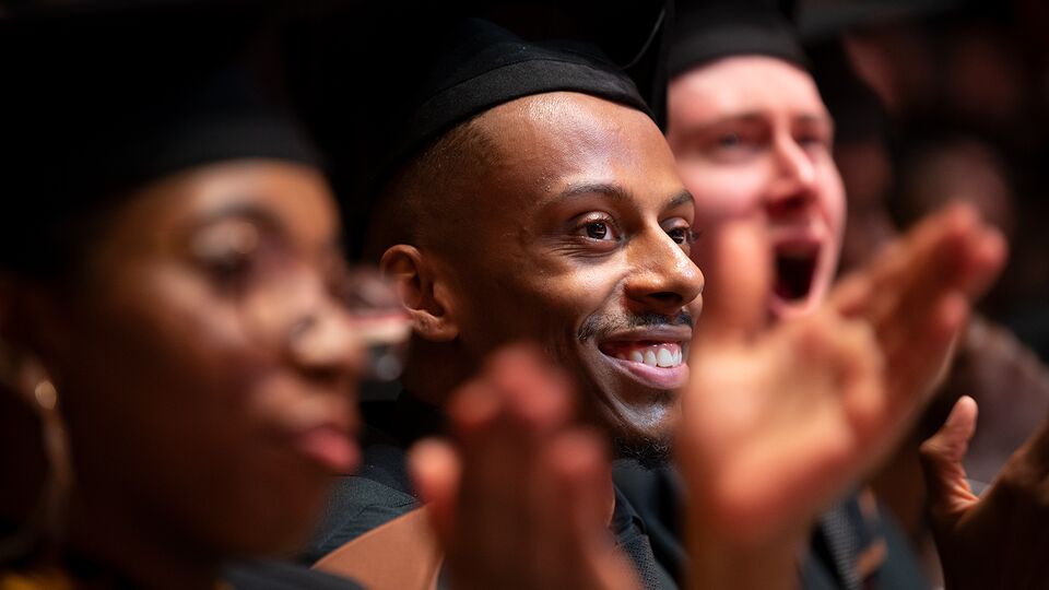 Students in mortarboards clapping at graduation ceremony