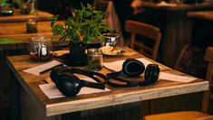 A pair of headphones rest on a wooden table with two cups of tea and a mint plant. 