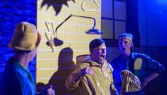 An actor on stage in a yellow raincoat under a shower