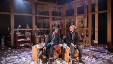 Two students sitting on bookcases on stage, surrounded by torn paper from books