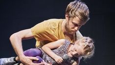 A photograph from Fevered Sleep’s Men & Girls Dance where a man cradles a young girl in his arms, lifting her off the floor.