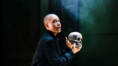 Alum Cush Jumbo on stage in Hamlet at The Young Vic, shrouded in mist she holds up a skull