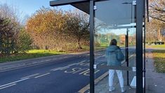 A clear bus stop shelter, with a person in the background
