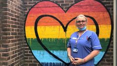 A medical professional standing in front of a rainbow heart mural