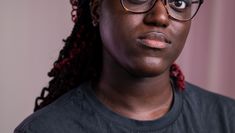 A profile photo of a dark skinned black woman with brown eyes and red and black hair wearing glasses and a black t-shirt