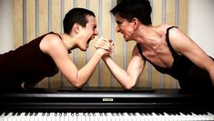 Two performers arm wrestle on a piano