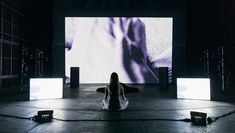 Performer sits with back to audience in front of large screen