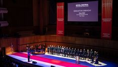 Central students perform on the Royal Festival Hall stage. A large screen at the back of the stage has the Central logo and words 'Graduation Ceremony Class of 2022'