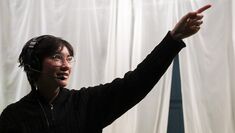 A student in a microphone headpiece points upwards against a white sheet