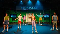 Actors performing on stage wearing gym clothing, beneath a screen displaying the word STRONGER
