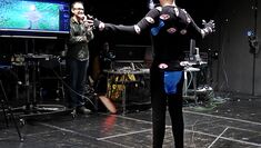 A performer stands in MOCAP suit with arm spread