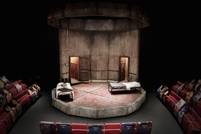 A set with two small beds, with doors behind them on either side of the stage
