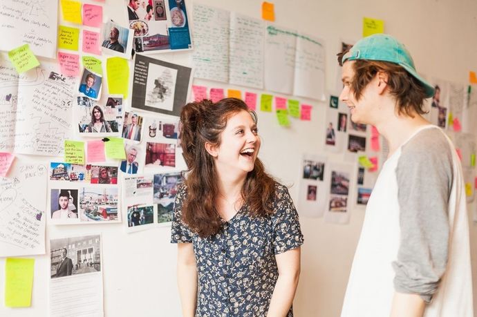 Two young people talking in front of a mood board wall