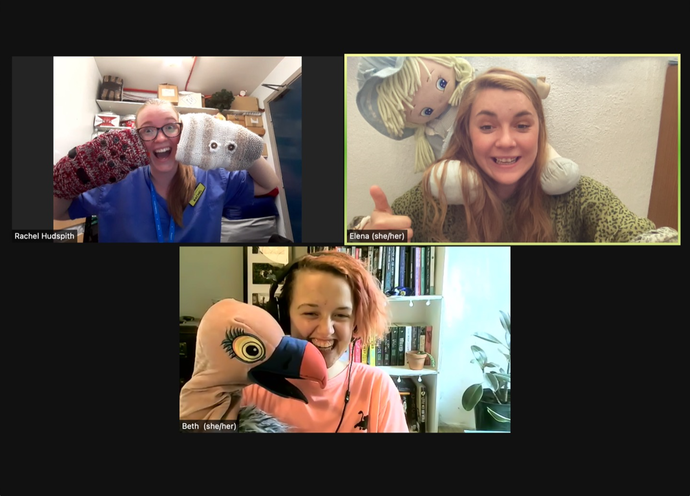 Three women on zoom call. They are all smiling. One woman is holding a bird puppet, another has a doll sat on her shoulder. The final woman is holding two twiddle muffs next to her face and grinning. 