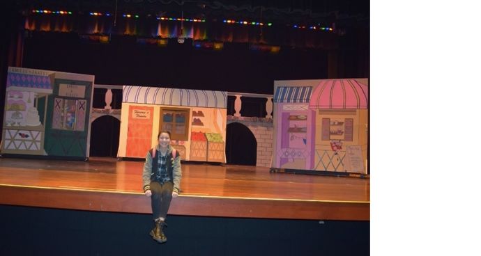 A photo of Melody Fritz sitting on a stage showcasing stage design that she's worked on