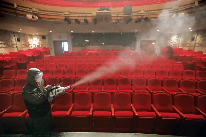 A person disinfecting a theatre with red, plush seats